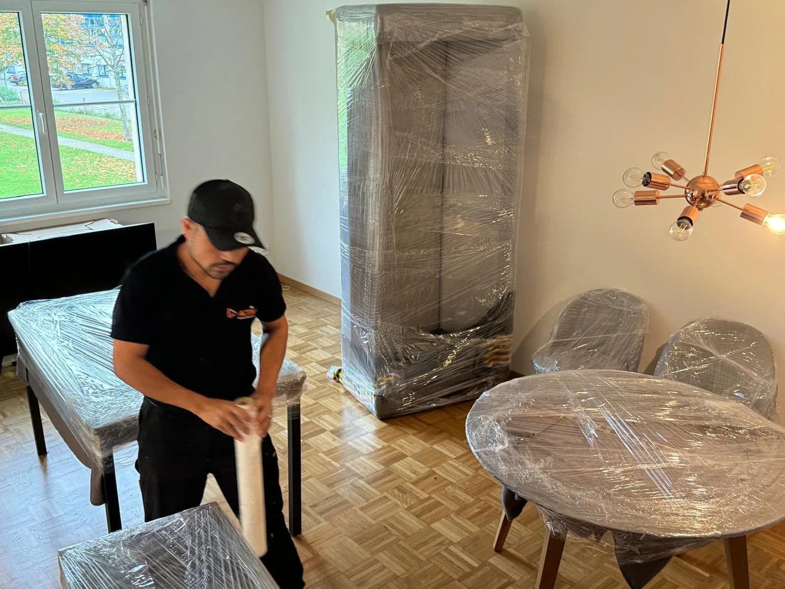 Mitarbeiter von Activ Umzüge wickelt Möbel in Schutzfolie ein, Schrank und Tisch bereits verpackt
